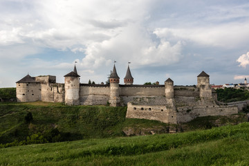 Fototapeta na wymiar A view on the side of the medieval Kamianets-Podilskyi fortress of the XVI century, located on a rocky green hill, under a beautiful cloudy sky. Ukraine.