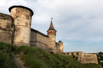 Fototapeta na wymiar Three towers and stone walls of the medieval fortress of the XVI century in the city of Kamianets-Podilskyi on the background of blue sky with birds. Ukraine.