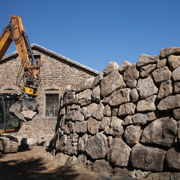 Construction d'un mur par enrochement de grosses pierres soulevées par une pelle mécanique