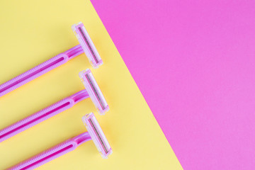 Three women's razors pink on an isolated pink and yellow background.