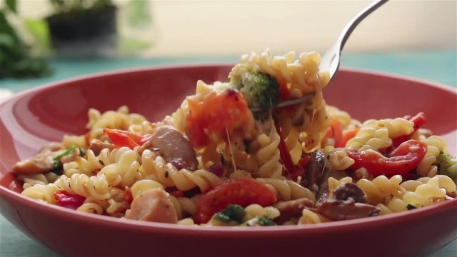 someone eat fusilli pasta with vegetables and melting cheese extreme close up