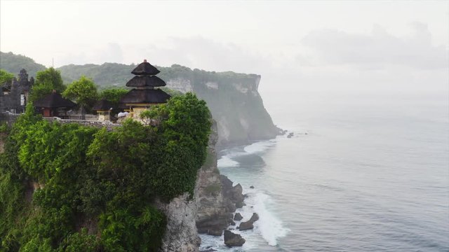 Breathtaking zooming out aerial view of Pura (Luhur) Uluwatu temple on the top of high cliff in the Indian ocean. A long coastline is on the background. Bali, indonesia