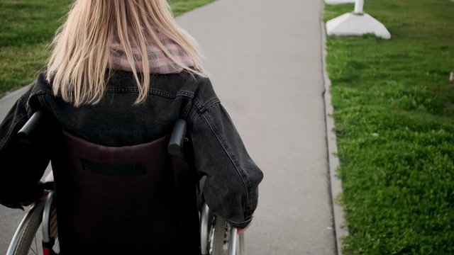 Disabled woman is moving in invalid carriage outdoors, close-up of body
