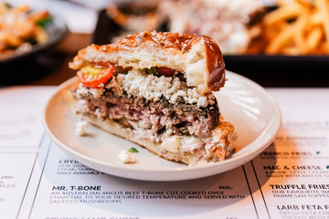 Close up cut half of Cheeseburger with grilled beef, feta cheese and sliced tomato served in white plate.