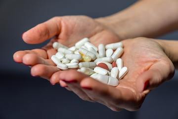 Both hands of a female girl with red fingernails holding many colorful pills and tablets as medicine and supplement for good health on grey background