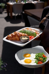Breakfast is set. Whole grain sandwich with fried egg, vegetables and herbs in the hands of a waitress. Serving food to customers.