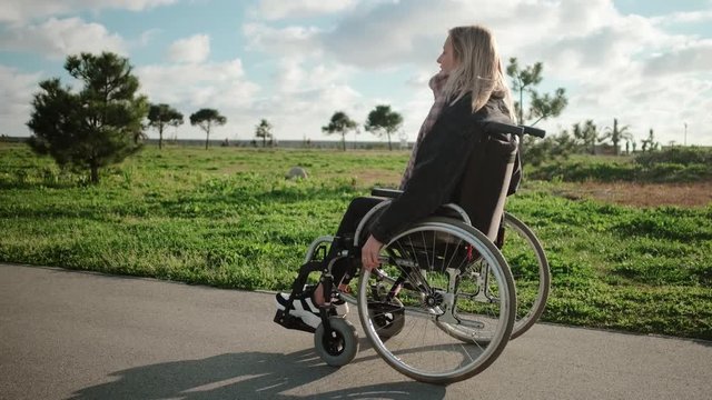 Young woman is sitting in invalid carriage and moving in park area