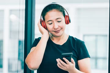 Foto op Plexiglas Young middle-aged athletes are listening to music from smartphones using wireless headphones after she is tired of exercising at the fitness center. Concepts about health and leisure care. © krumanop