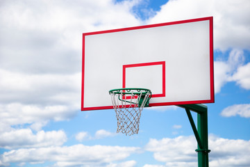 Basketball hoop on the street with blue cloudy sky on the background. Outdoor sport activity and streetball concept.