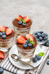 Classic tiramisu dessert with blueberries and strawberries in a glass on concrete background