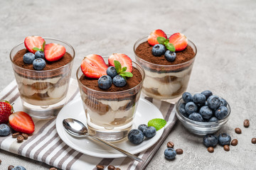 Classic tiramisu dessert with blueberries and strawberries in a glass on concrete background