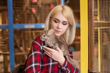 A beautiful blond woman holding a gray chinchilla in her hands. Mammal, rodent. Contact zoo.