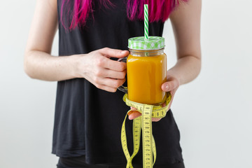 Unidentified young girl hipster holding a fruity protein juice with a straw and measuring tape. Conception of healthy nutrition and good fitness.