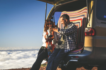 Couple of enjoying outdoor sitting on the back of a 4x4 van. Gorgeous mountain panorama on the background. Happy wife and husband drinking cups of coffee. Tourists enjoy a beautiful vacation together © Fabio Principe