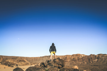 Teenager boy enjoying outdoors standing on a mountain cliff overlooking the Tenerife Teide National Park. Brave young male looking at the mountain panorama.  Adventure carefree relax and youth concept
