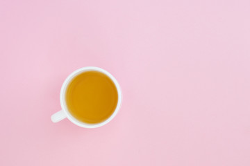 A white cup with chamomile tea on pink background, top view