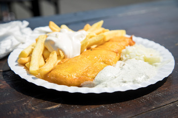 Seelachs Backfisch im Bierteig mit Remoulade, Pommes, Mayonnaise und Krautsalat draußen auf Pappteller und Holztisch 