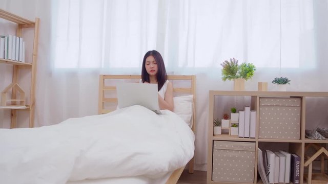 Young business freelance Asian woman working on laptop checking social media while lying on the bed when relax in bedroom at home. Lifestyle women at house concept.