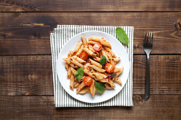 Italian pasta with tomatoes and spinach on wood table.