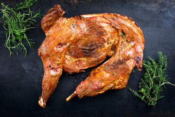 Barbecue half of dairy goat with shoulder and leg garnished with a bouquet garni as top view on an old rustic board