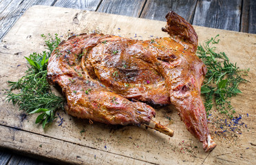 Gegrilltes halbes Milch Zicklein mit Schulter und Keule garniert mit Bouquet Garni Kräuter als Draufsicht auf einem alten rustikalen Schneidebrett