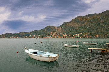 Fototapeta na wymiar Cloudy autumn landscape - mountains, sea, and fishing boats on the water. Montenegro, Adriatic Sea, view of Bay of Kotor near Verige Strait