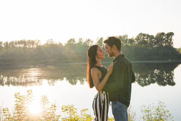 Romantic and people concept - young couple hugging together near the river or lake and enjoying summer time