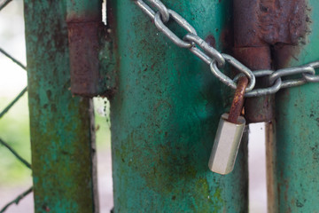 Closed green old gate with a rusty padlock and metal chain