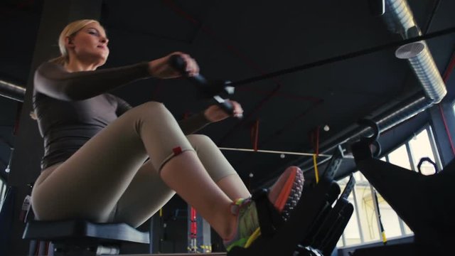 professional sportswoman sits on rowing machine slides seat pulls oar and strengthens muscles low angle shot close view