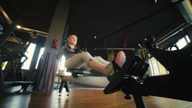 handsome bald man and pretty blonde woman train actively on rowing machines in gym low angle shot close view