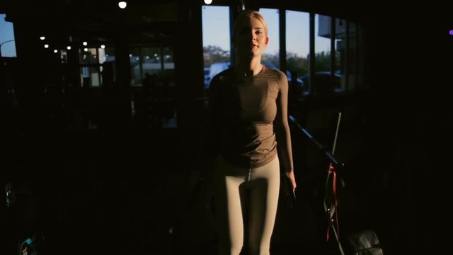 pretty blonde woman in trendy sportswear performs box step up in professional gym crossfit zone at sunset light closeup