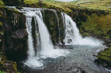 Fototapeta premium The waterfall of Kirkjufell in Iceland. Clear water falling into the stream. Beautiful scenery on a cold grey afternoon.