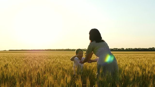The happy son runs into his mother's arms around a wheat field during sunset, the mother hugs and kisses the child