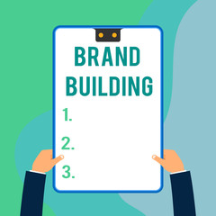 Conceptual hand writing showing Brand Building. Concept meaning Generating awareness Establishing and promoting company Two executive male hands electronic device geometrical background