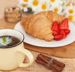 morning breakfast with a cup of delicious and hot black tea and croissants with chocolate and fresh fruit, strawberries on a plate. Food on beige background with flowers