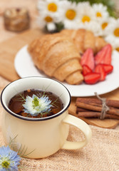 morning breakfast with a cup of delicious and hot black tea and croissants with chocolate and fresh fruit, strawberries on a plate. Food on beige background with flowers, vertical frame