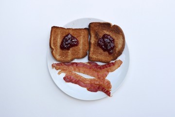 Breakfast smiley face of toast and bacon on a white plate against a white background