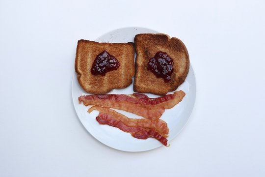 Breakfast smiley face of toast and bacon on a white plate against a white background