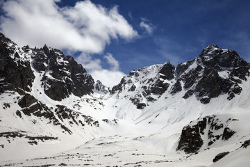 Snowy sunlit mountains with traces from avalanches and blue cloudy sky