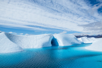 Warm weather melting the ice of the Matanuska Glacier into a large blue pool. An ice cave cuts into...
