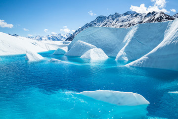 Mount Wickersham over a large blue pool with fins of ice protruding from the cold waters.