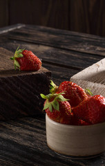 Composition on a wooden, dark background, consisting of fresh strawberries, which lies on the wooden bars of dark and light colors, in small ceramic cups.