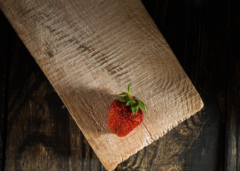 Composition consisting of a tree lying on a white bar, red strawberries on a dark, contrasting, wooden background, top view.