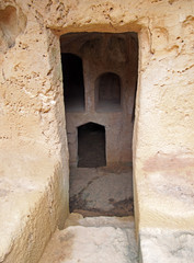 a narrow door carved into rock with steps leading to dark underground chambers at the tombs of the kings in paphos cyprus