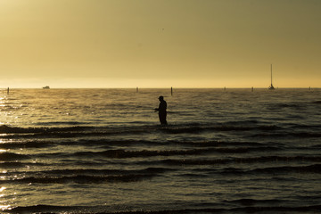 silhouette of a fisherman with a fishing rod in the sea