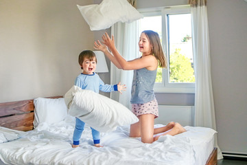 Kids pajama party. Two happy siblings playing and fighting with pillows jumping on bed in bedroom....