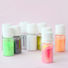Colorful glitters lies on pastel pink background. Many round jars with multi-colored bright sparkles for nail polish
