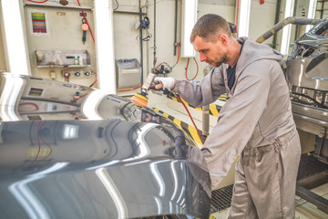 working in the paint shop at the car body, grinds painted surfaces.