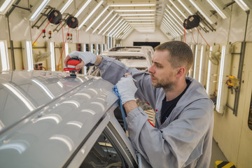 working in the paint shop at the car body, grinds painted surfaces.