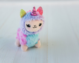 Colored plush llama unicorn on white wooden background